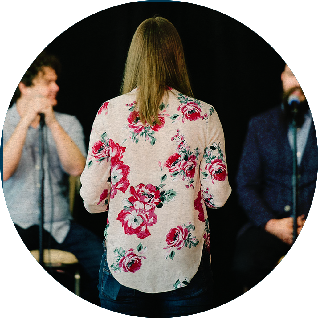 A person with their back facing the viewer, asking a question to Jesse Thorn and Jordan Morris, who are visible in the background, slightly out of focus.